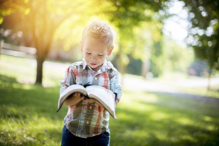 Closeup shot of a child holding an open bible while looking at it with a blurred background