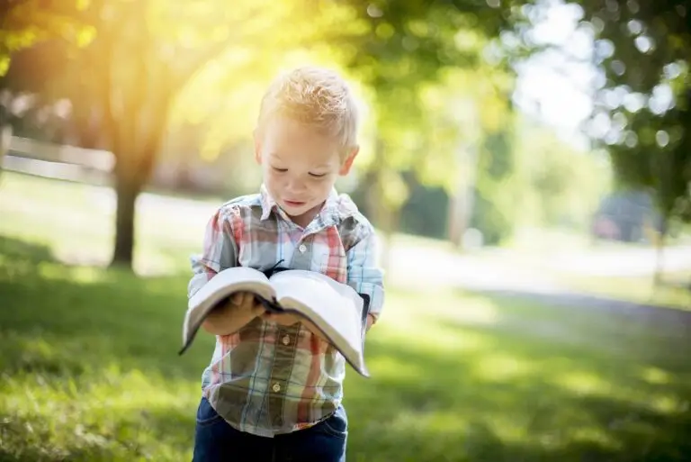 Closeup shot of a child holding an open bible while looking at it with a blurred background