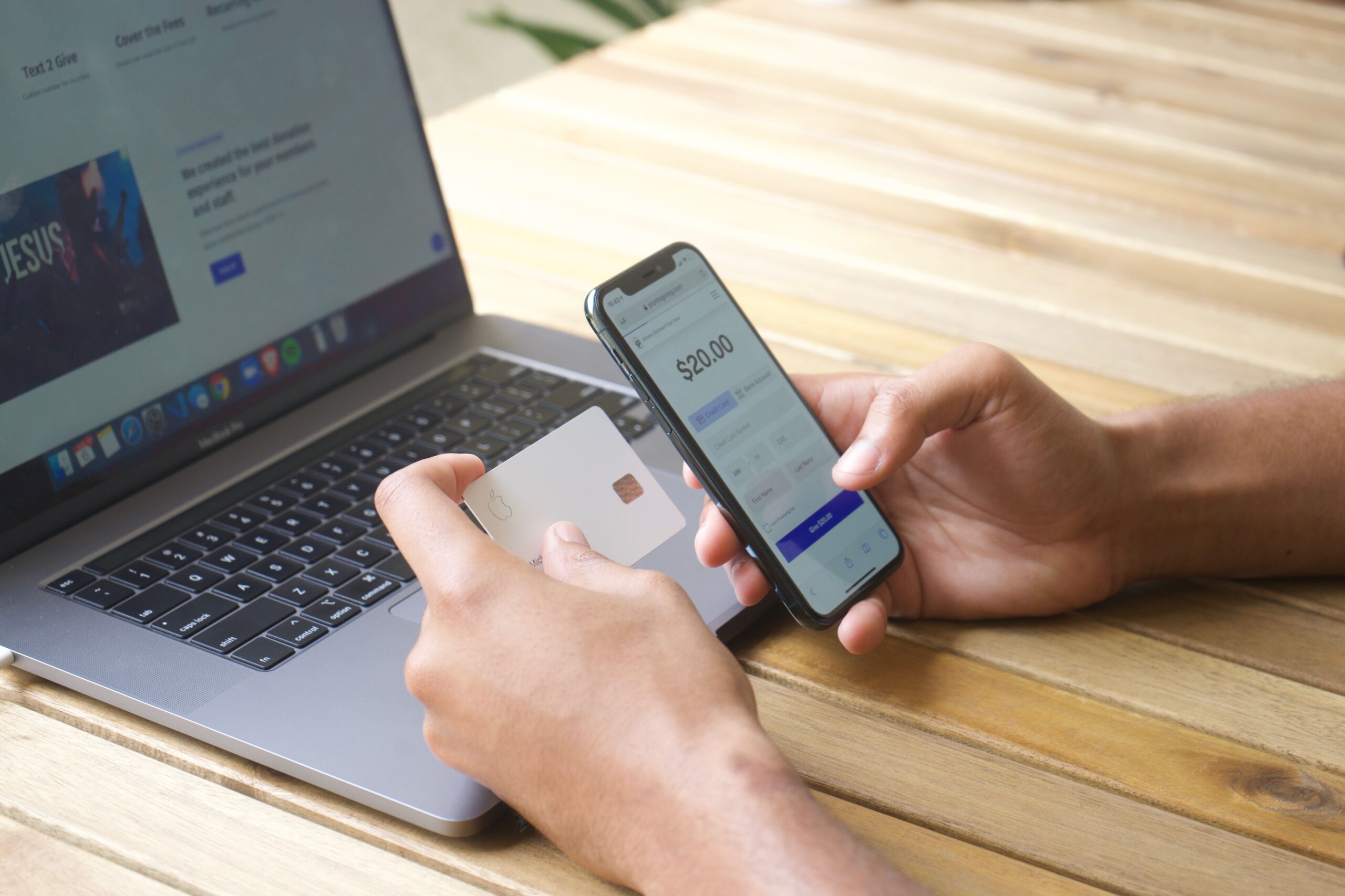 Person holding phone and credit card in front of a laptop, giving their tithe through a church app