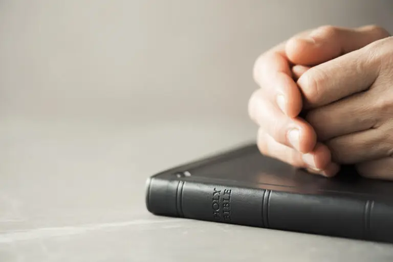 Hands closed in prayer on Holy Bible.