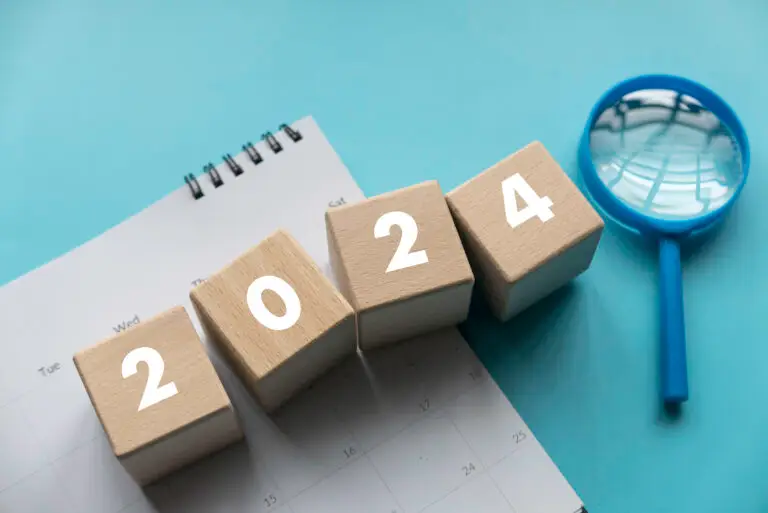 Magnifying glass and calendar with a wooden cubes with 2024 over a blue background.