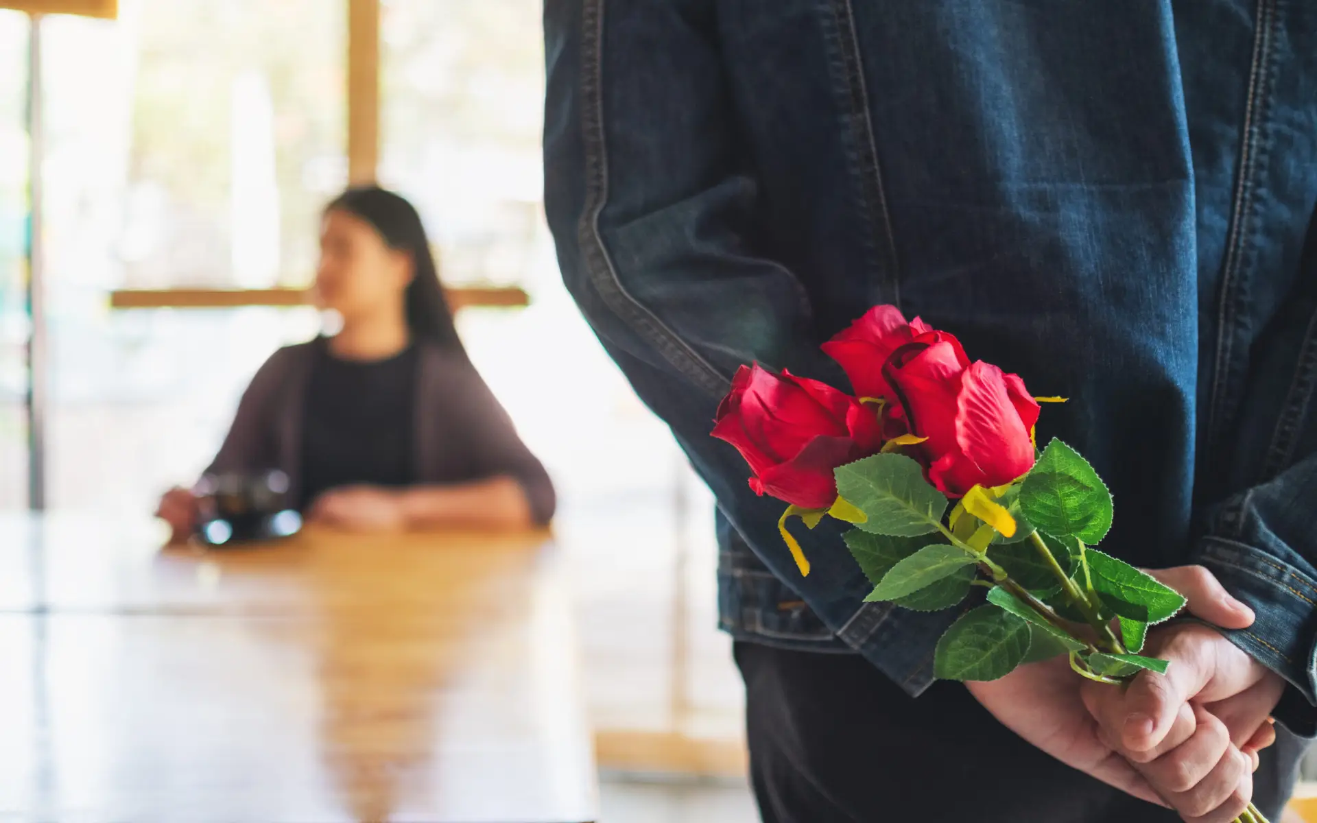 A man holding and hiding a red rose bouquet behind his back to surprise his bride