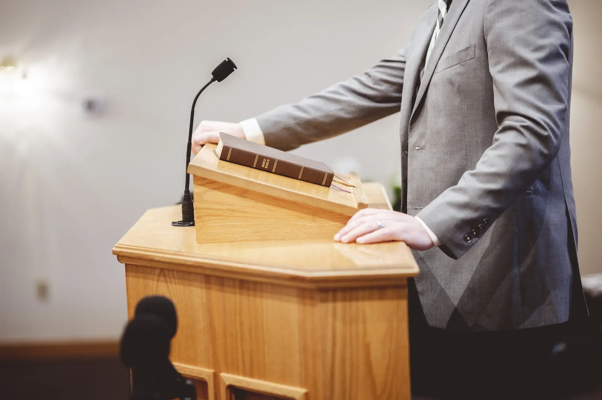 Side angle photo of pastor preaching from a wooden pulpit with a closed bible on top