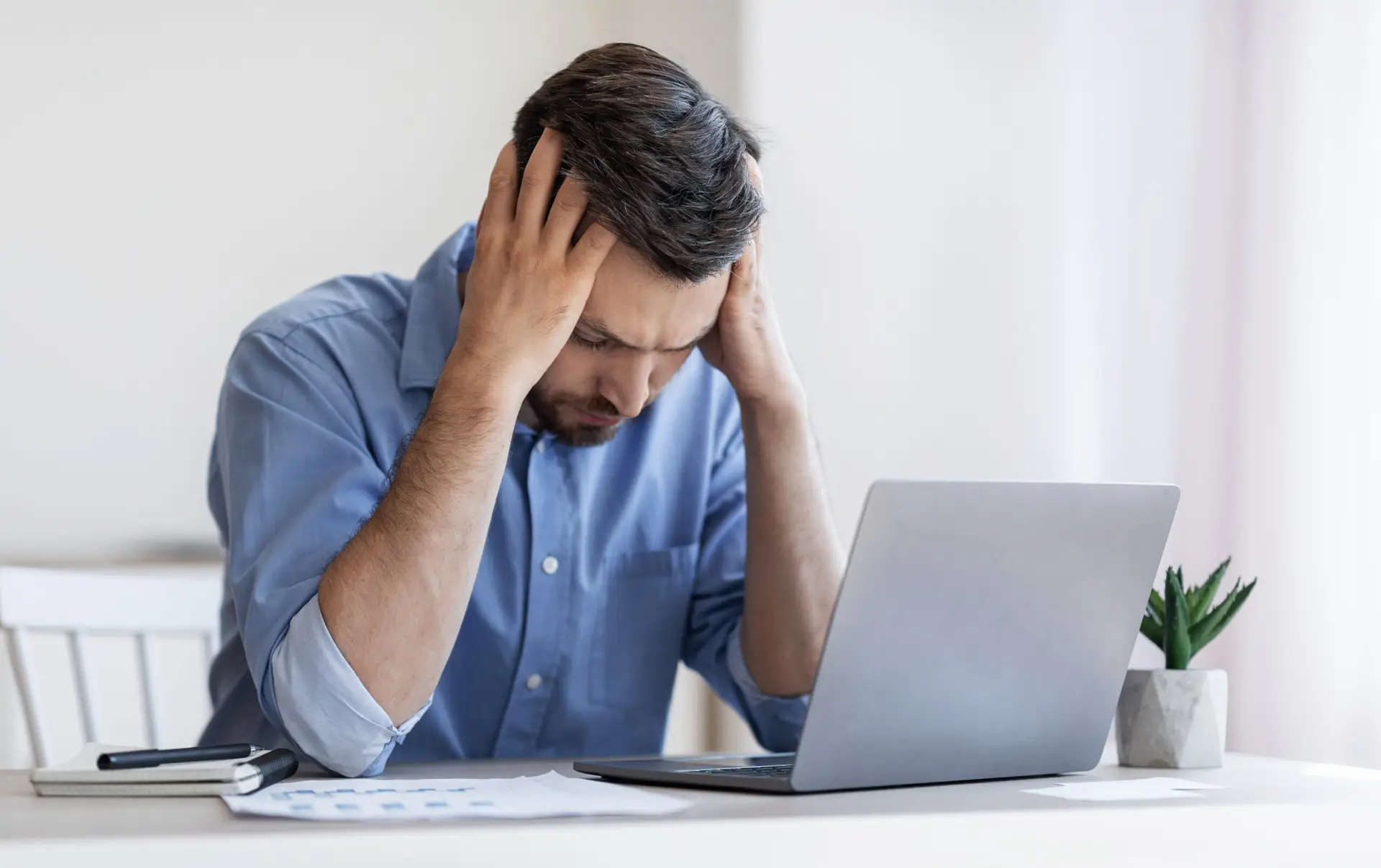 Man sitting in front of a laptop with hands on head frustrated