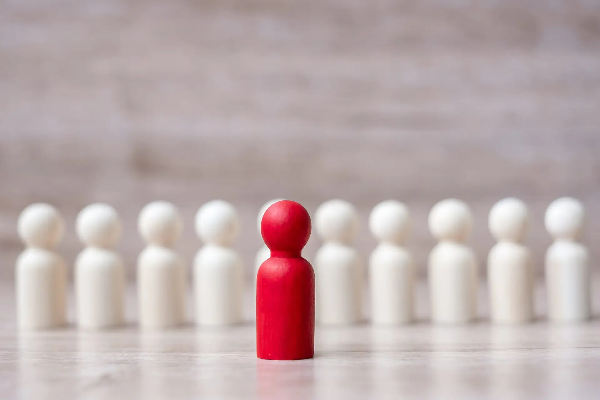 Red wooden man in front of row of white wooden men portraying concept of leadership