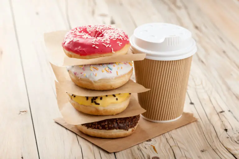 Colorful donuts stacked together and a disposable coffee cup on a wooden table