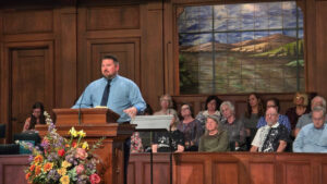 Andrew Brock preaches from a wooden pulpit with people seated in the choir loft behind him.