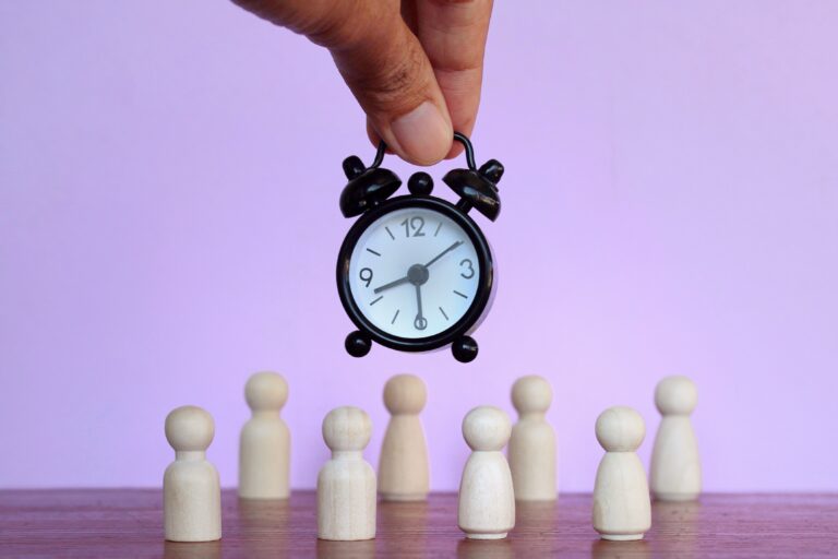 Alarm clock and wooden dolls on purple background.