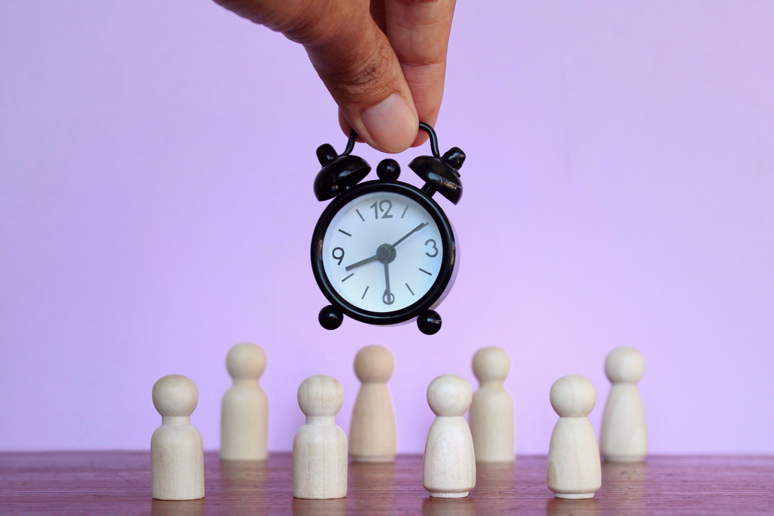 Alarm clock and wooden dolls on purple background.