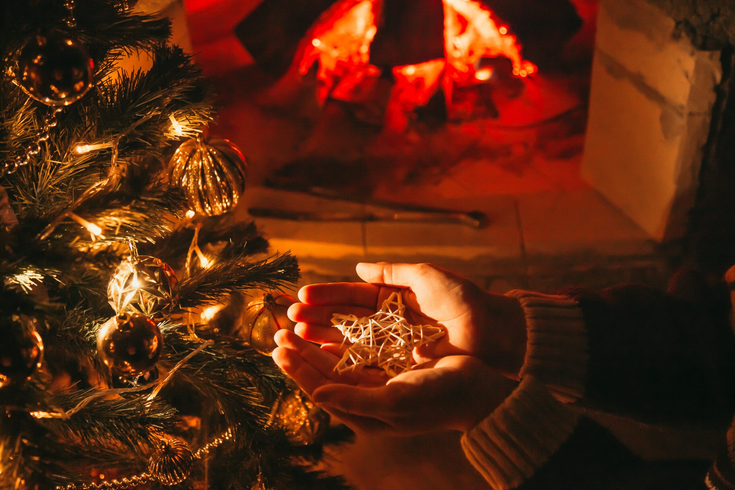 Woman holding a star sitting under the Christmas tree next to the fireplace.