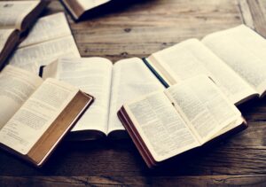 A high-angle shot showcases multiple open books and Bibles on a rustic wooden table.