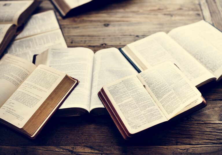 A high-angle shot showcases multiple open books and Bibles on a rustic wooden table.